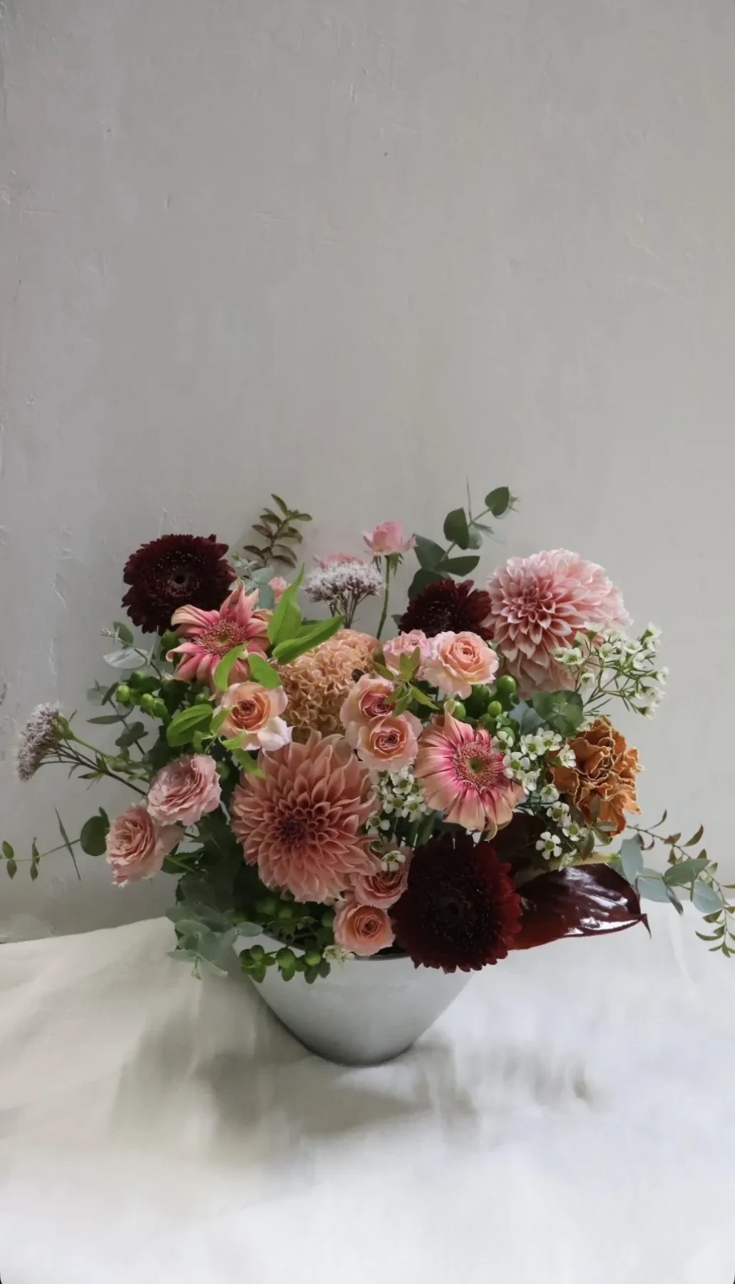ピンクと深い赤の花を白い器に活けたアレンジメント
